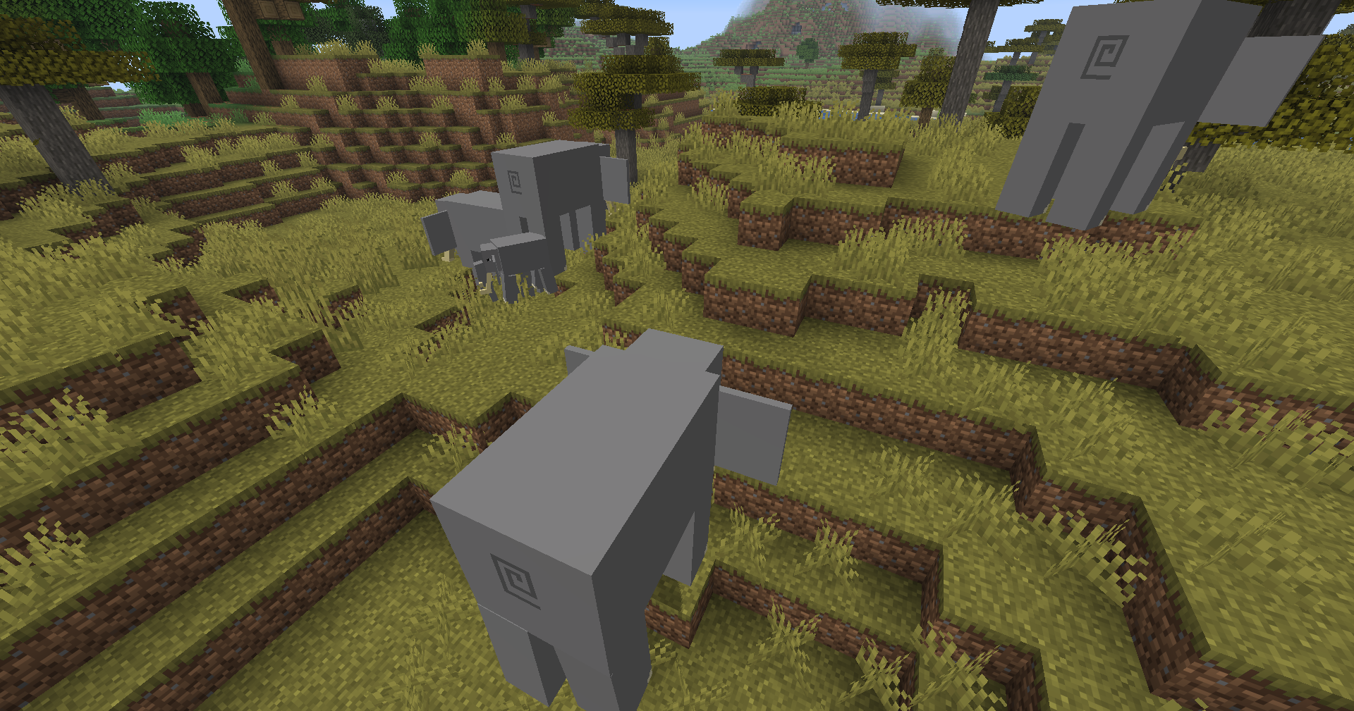 Minecraft savanna screenshot with several elephants standing in tall grass.